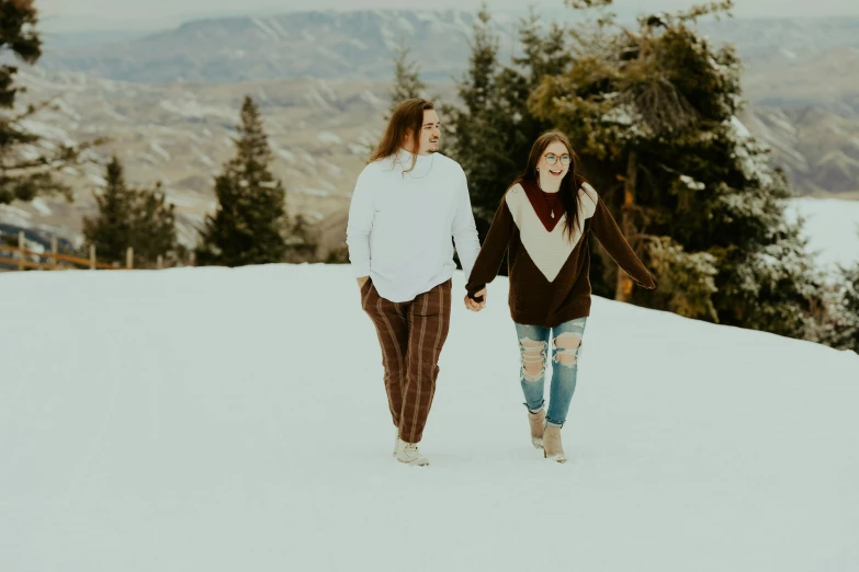 a couple walking together in the snow with trees behind them