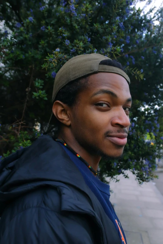 a man with a beanie standing in front of a tree