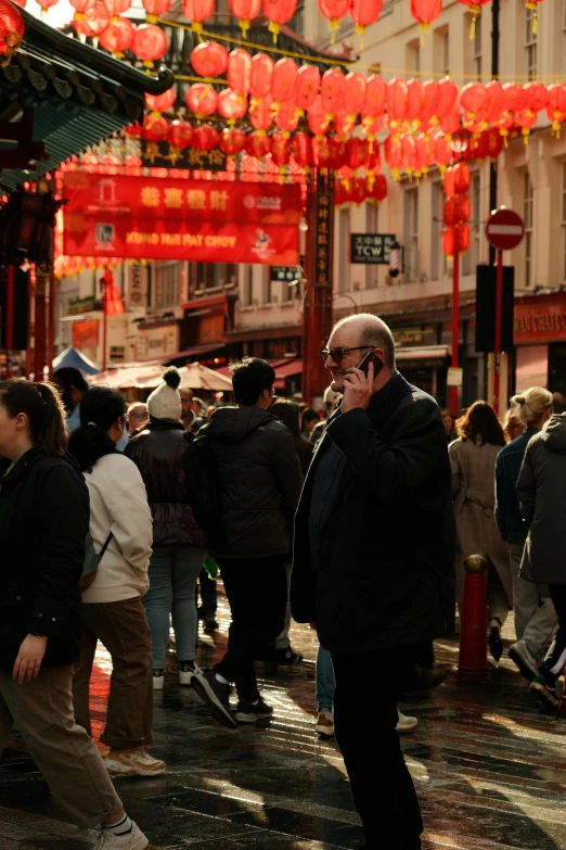 an older man in a black jacket walking with other people on a busy street