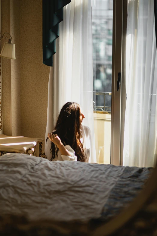 woman sitting in the shadows of her bedroom looking out the window