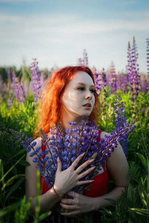 a woman with red hair wearing white makeup holds a bouquet of lavender flowers