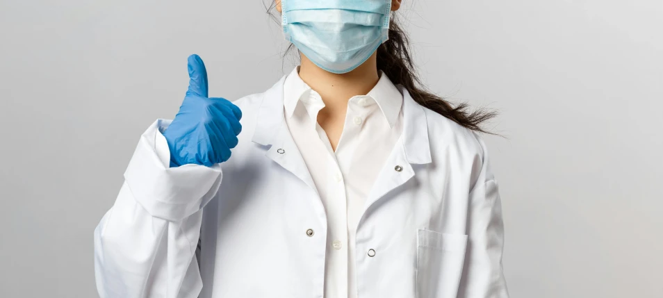 a woman wearing a surgical mask shows a thumb up sign