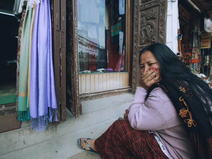 a woman sits outside of a store smoking a cigarette