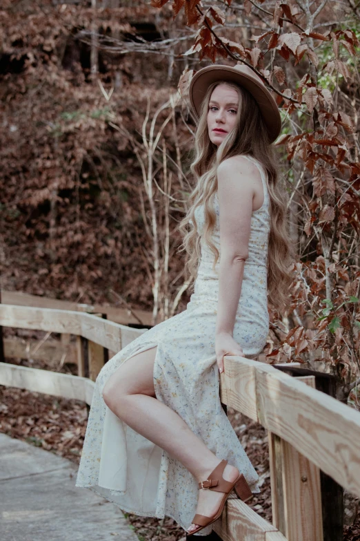 woman in a dress and hat is sitting on a fence