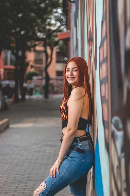 an attractive red headed woman leaning against a blue wall