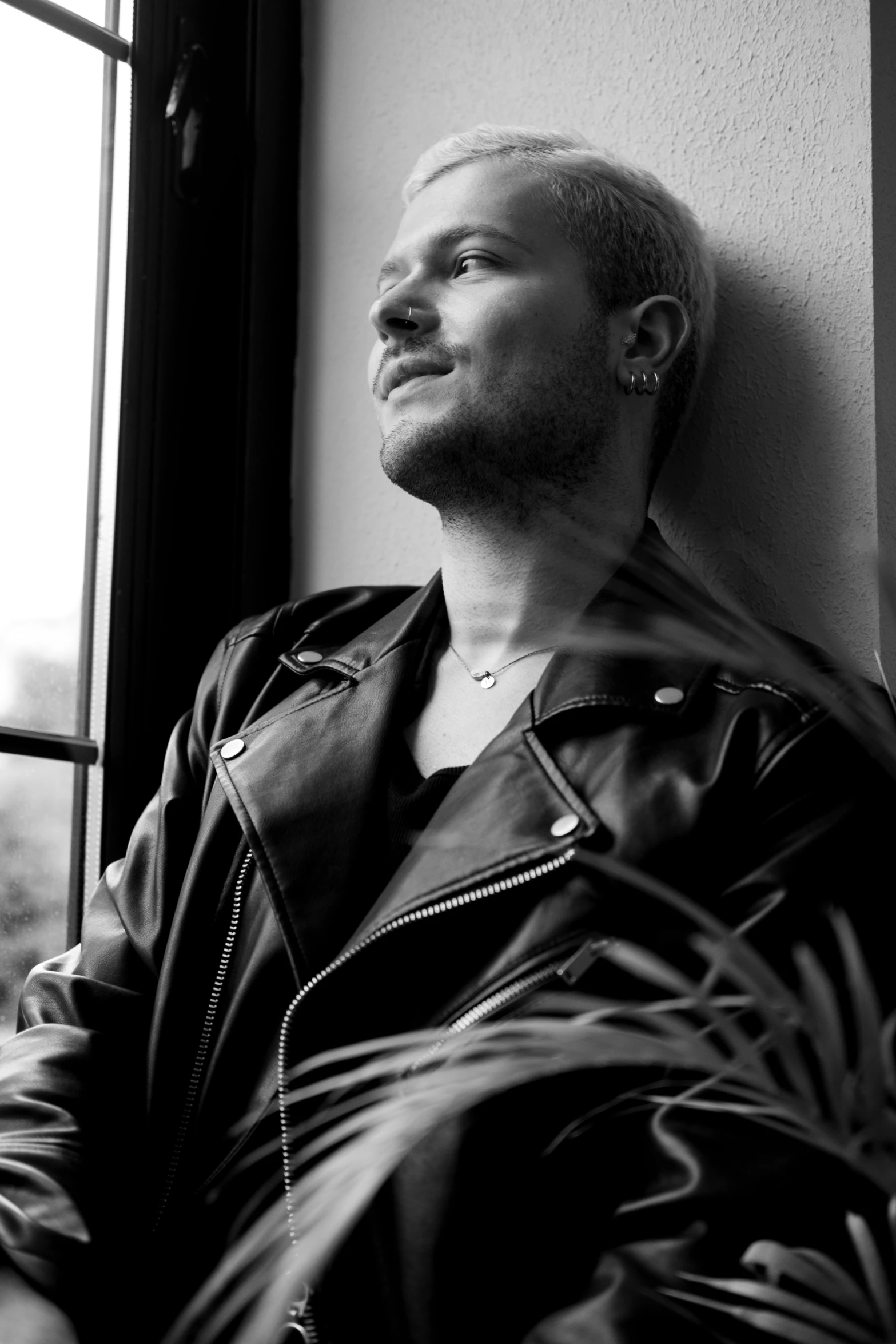 a young man leans against a wall next to a window