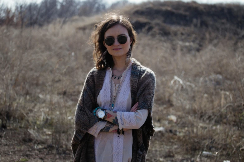 a woman standing in front of a hill wearing sunglasses