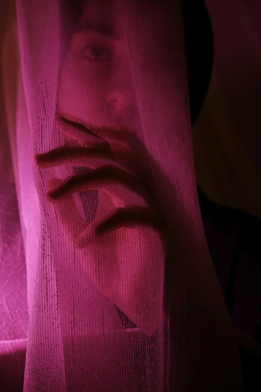 a very close up s of someone hiding behind a pink curtain