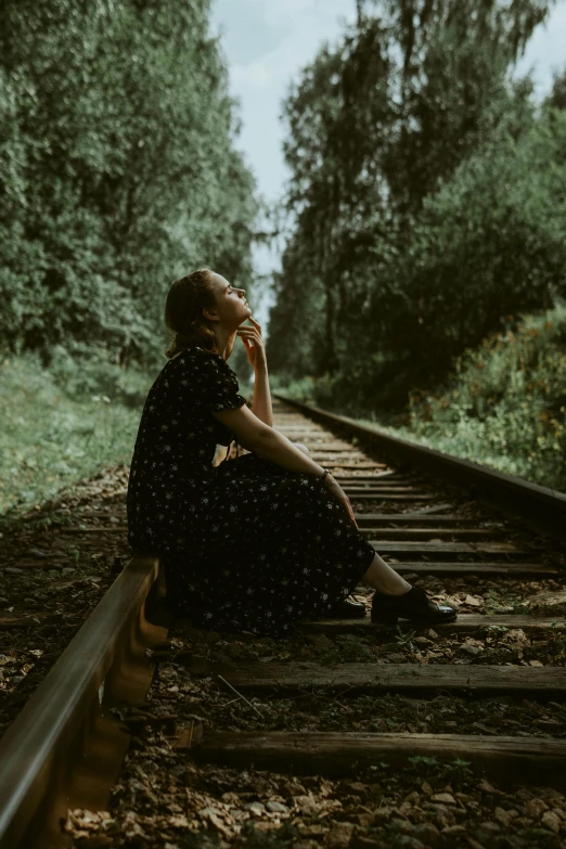 a woman sits alone on the railroad tracks