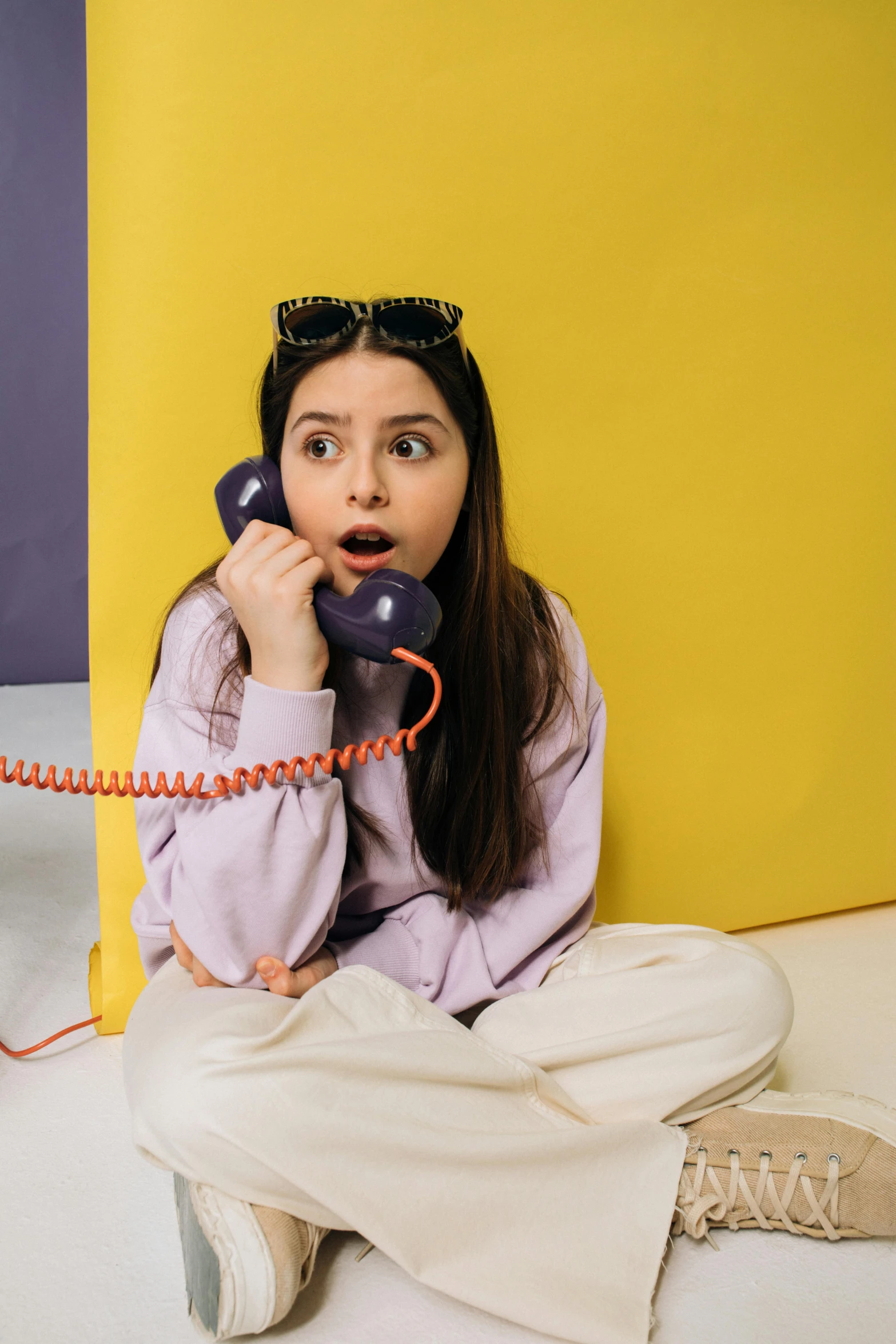 a woman holding an old - fashioned phone sitting next to a yellow and gray wall