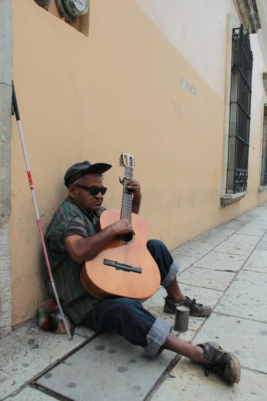 a man sitting against a wall holding an acoustic guitar