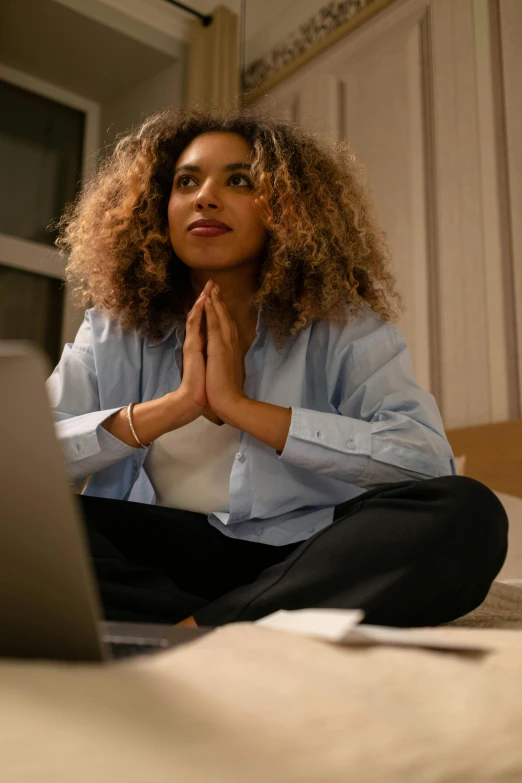 a woman sitting on the floor while meditating while using her laptop