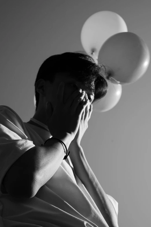 man holding three balloons while covering his face