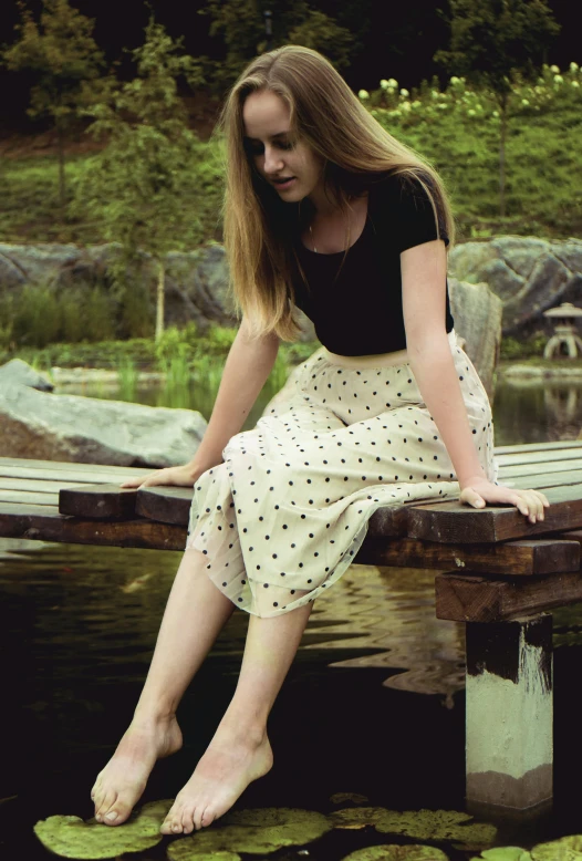 the woman is sitting on a wooden pier in her dress