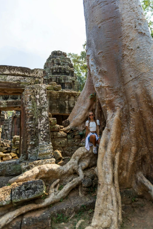 a woman sits on top of a tree in front of ruins