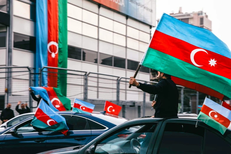 a person holds up flags in front of cars