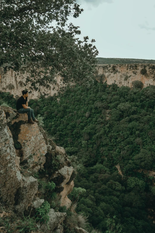 man sitting on the edge of a cliff while looking out into the distance