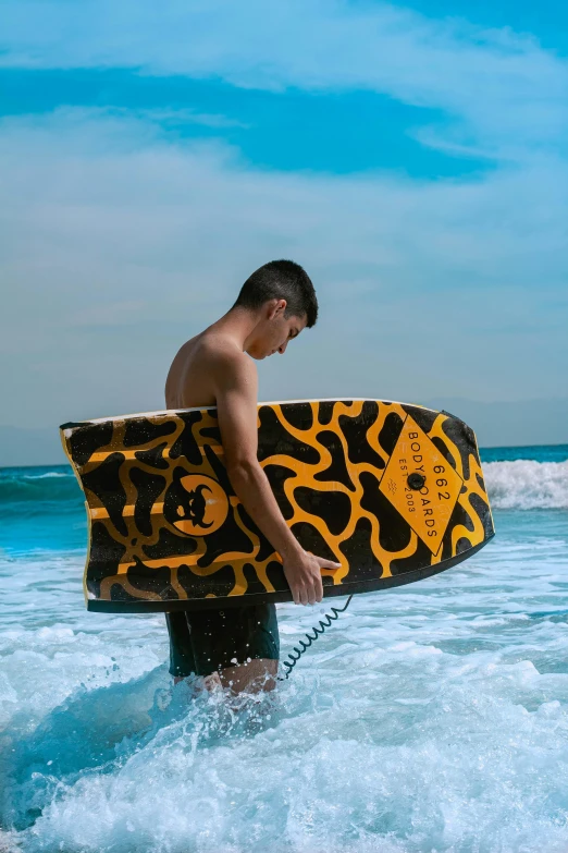 a shirtless young man carrying his surfboard into the water