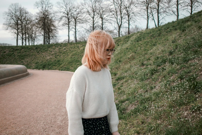 a red haired woman in glasses and white sweater standing by a path
