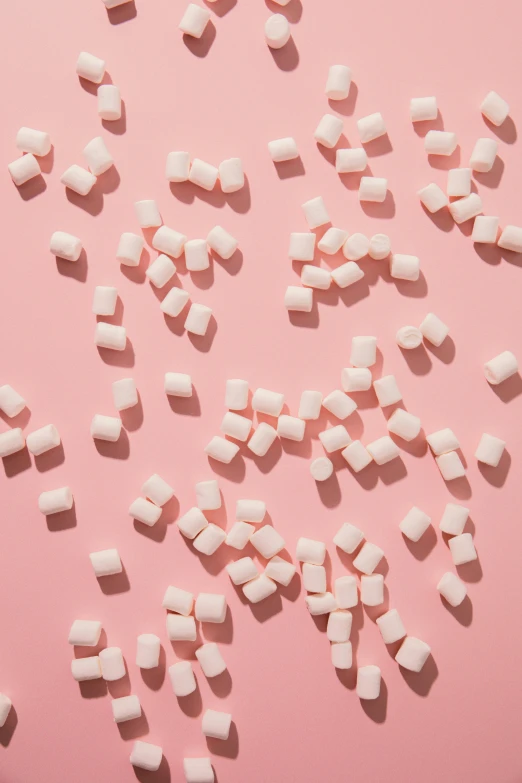 a pink background is covered with white chunks of marshmallows