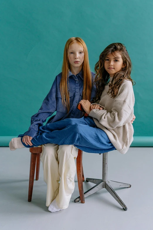 two girls sitting in chair against a teal wall