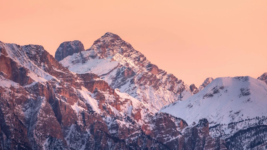 the mountain side is covered with snow in pink sunlight