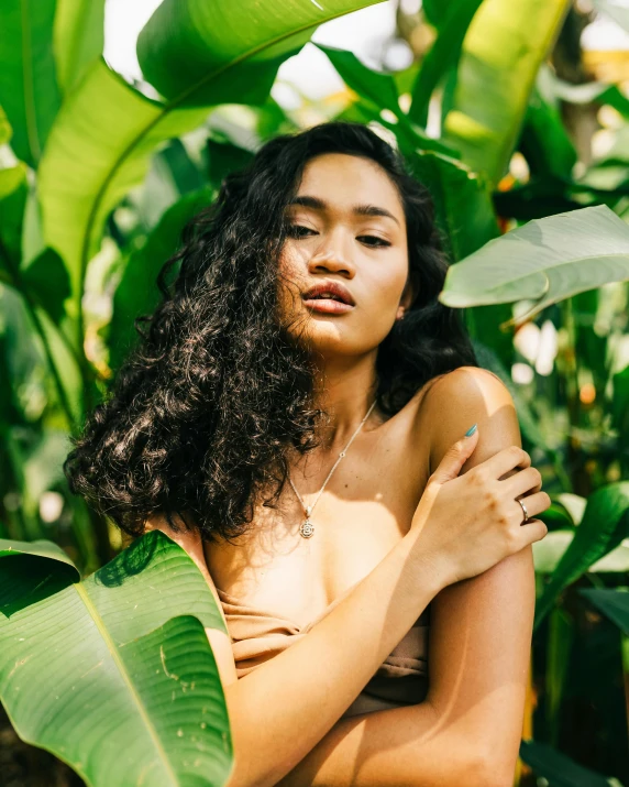 a woman is standing with her shirt off near green leaves