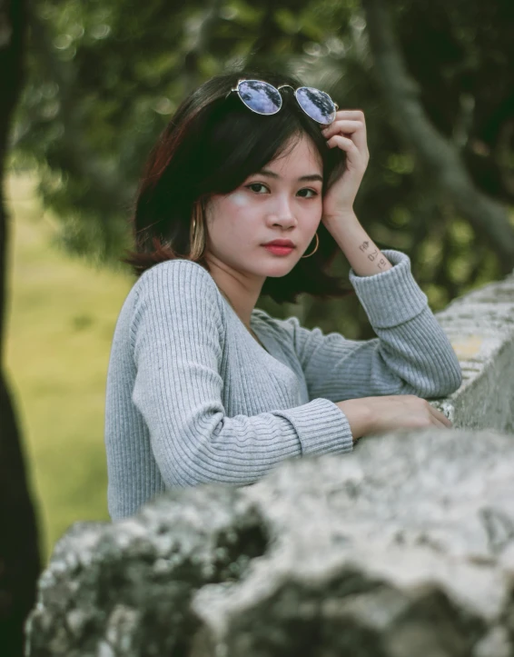 asian woman with glasses leaning against a rock