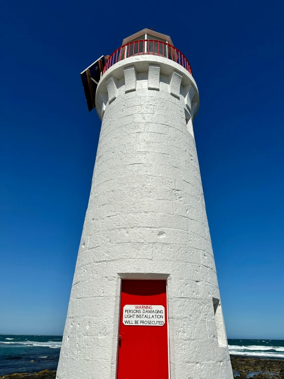 a white lighthouse with a red door in front of the ocean