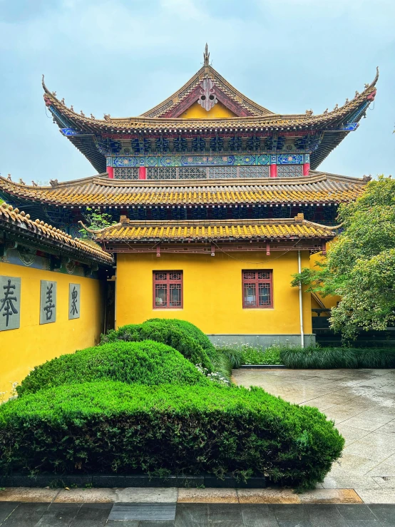 a yellow house in front of a green bush