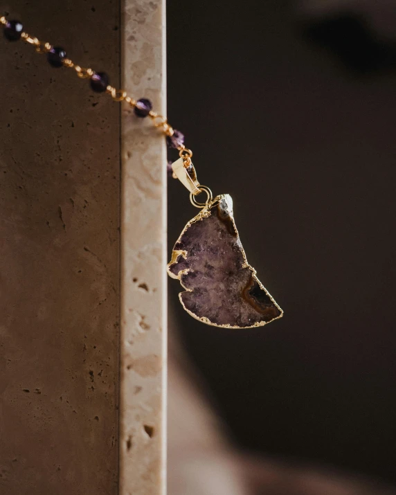 a close up view of a necklace with a large purple stone hanging from a golden chain