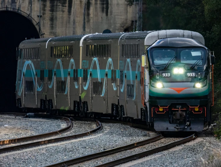 a green train is coming out of a tunnel