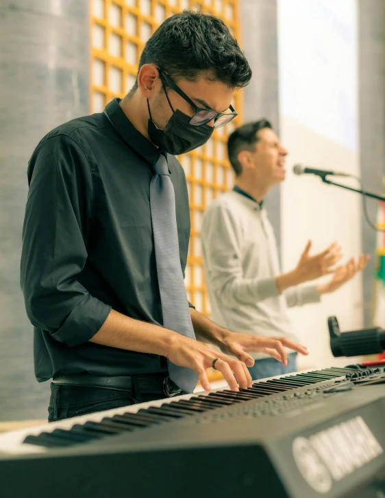 a man in a tie and a man wearing a mask standing near a keyboard