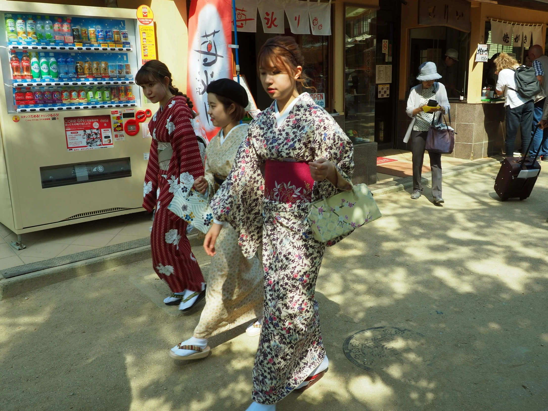 several geisha walking on the street with many vending machines