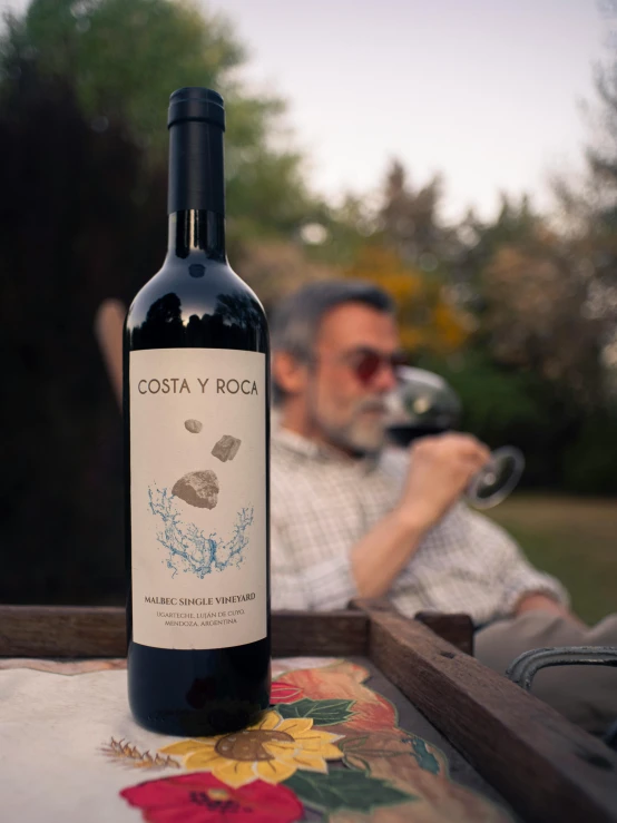 a man sitting in front of a bottle of wine on top of a table