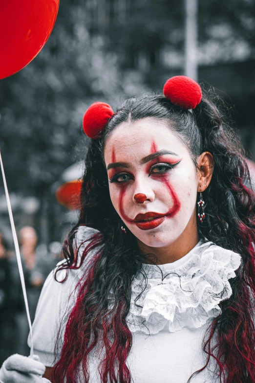 a woman wearing a white and red clown makeup holds a balloon