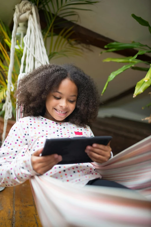 little girl using a tablet computer on a hammock