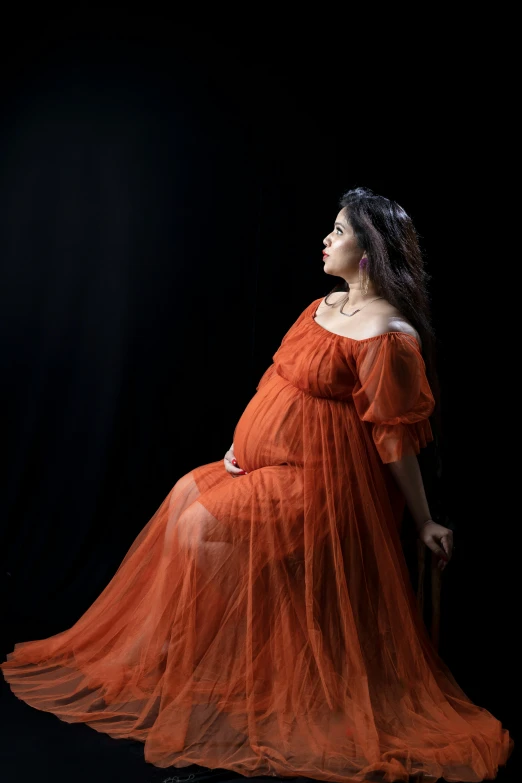 a woman is dressed in an orange dress sitting on a black background