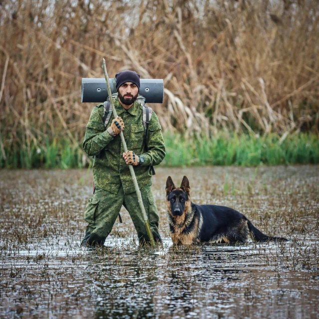 man walking through flooded field with dog carrying equipment on back