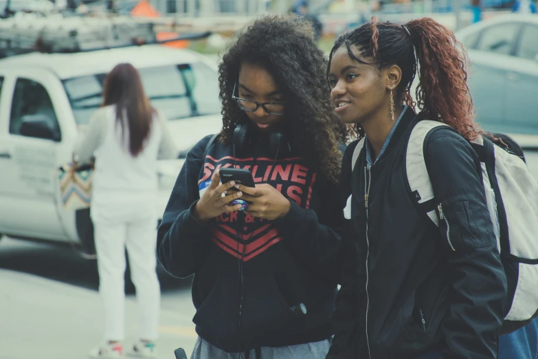 two girls using their cell phones on the sidewalk