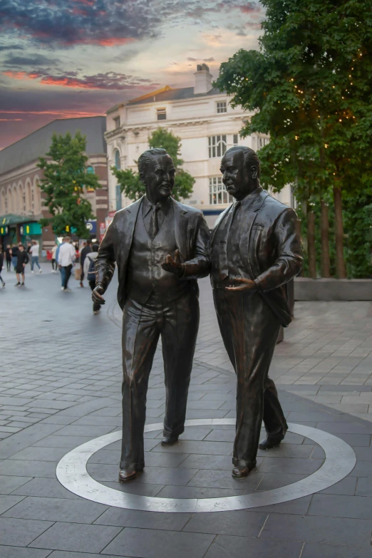 two statues are in the center of a circular area on the sidewalk, in front of a sunset