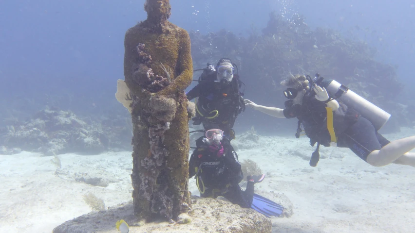 three divers in the water by a statue