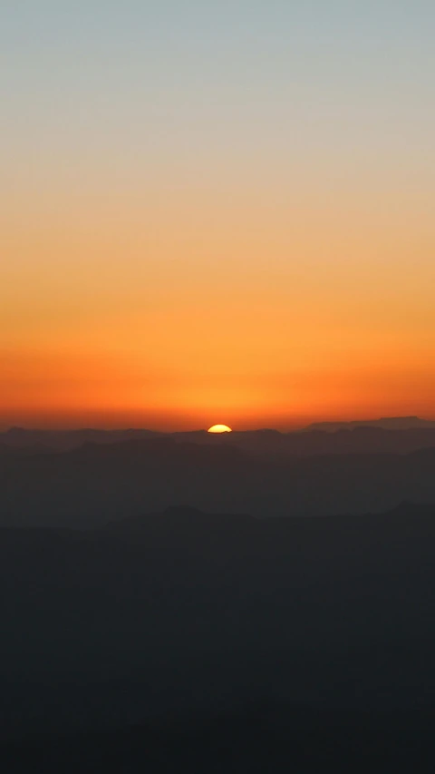 a large orange and yellow sun setting over mountains