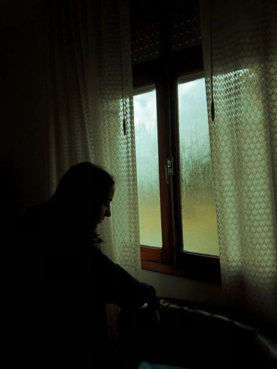 a person sitting next to a window while rain drops on the glass