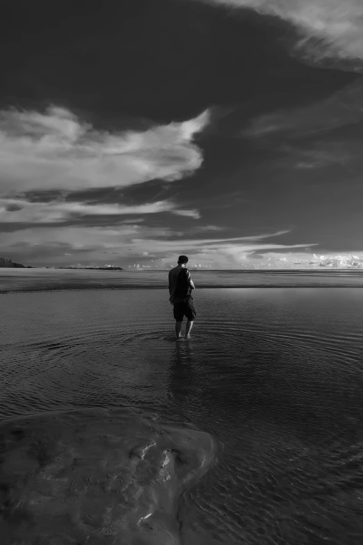 person walking alone in shallow water at sunset