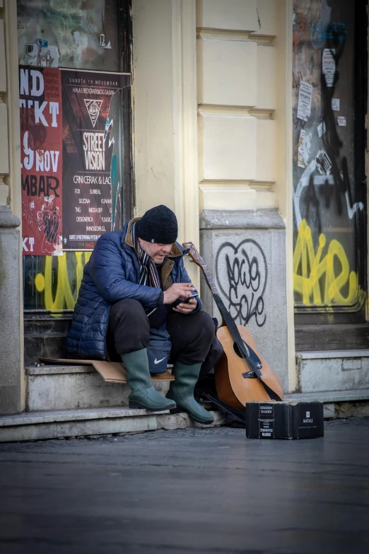 the man is sitting on the corner and playing his guitar