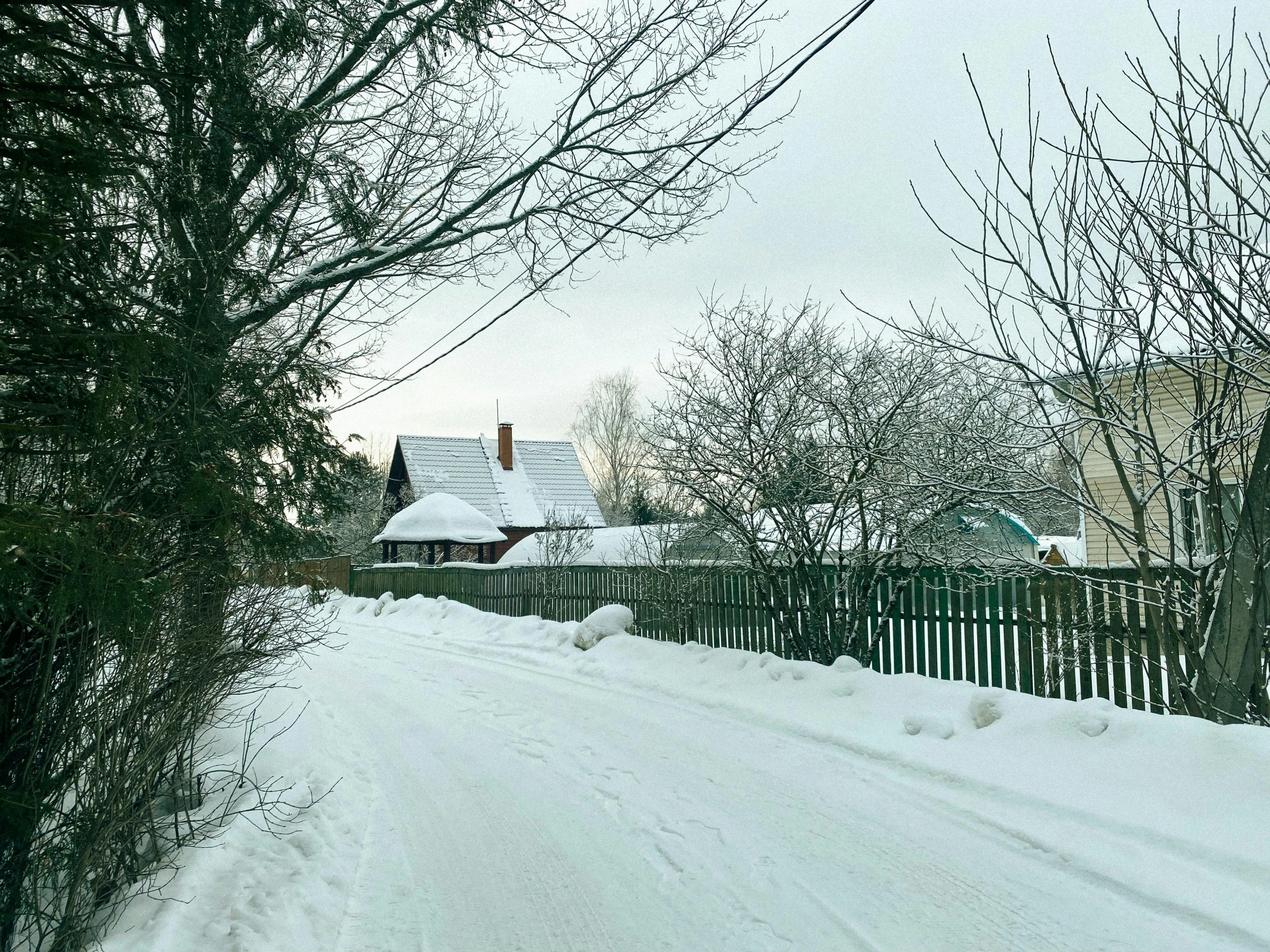 snow covers an alley and street, and there is a black fence between it