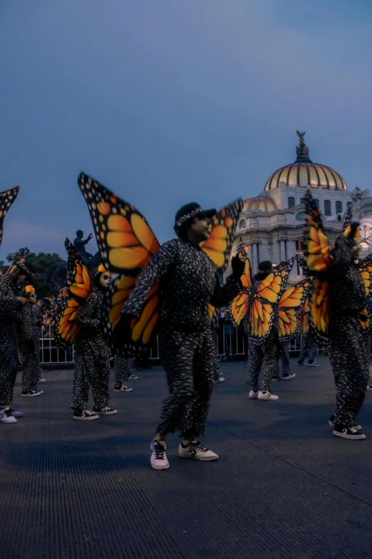 group of people in fancy erfly costumes with white buildings behind them