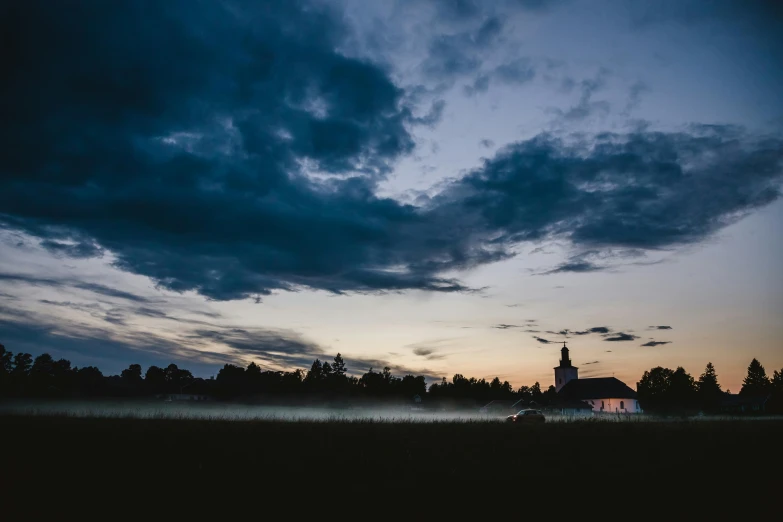 a field at dusk with a church and cloudy skies