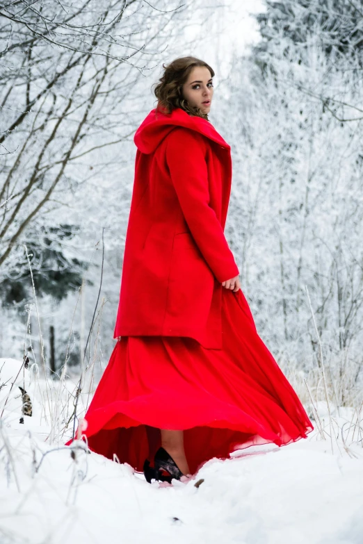 a woman standing in the snow wearing a red coat